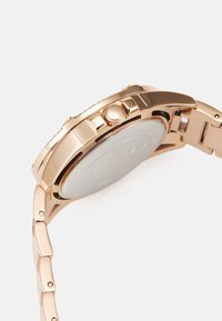 Orologio in metallo oro rosa con cassa rotonda, corona texturizzata e bracciale a maglie con bordi lucidati e retro in argento liscio.