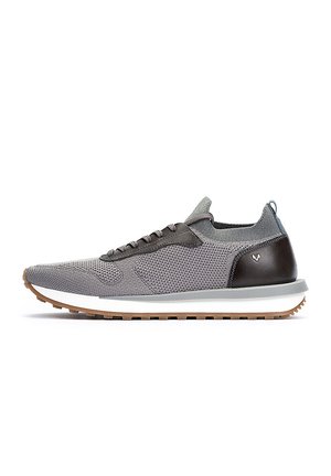 Zapatilla atlética gris de punto con acentos de cuero marrón oscuro, una entresuela blanca y una suela de goma texturizada. Presenta cordones negros y una lengüeta.