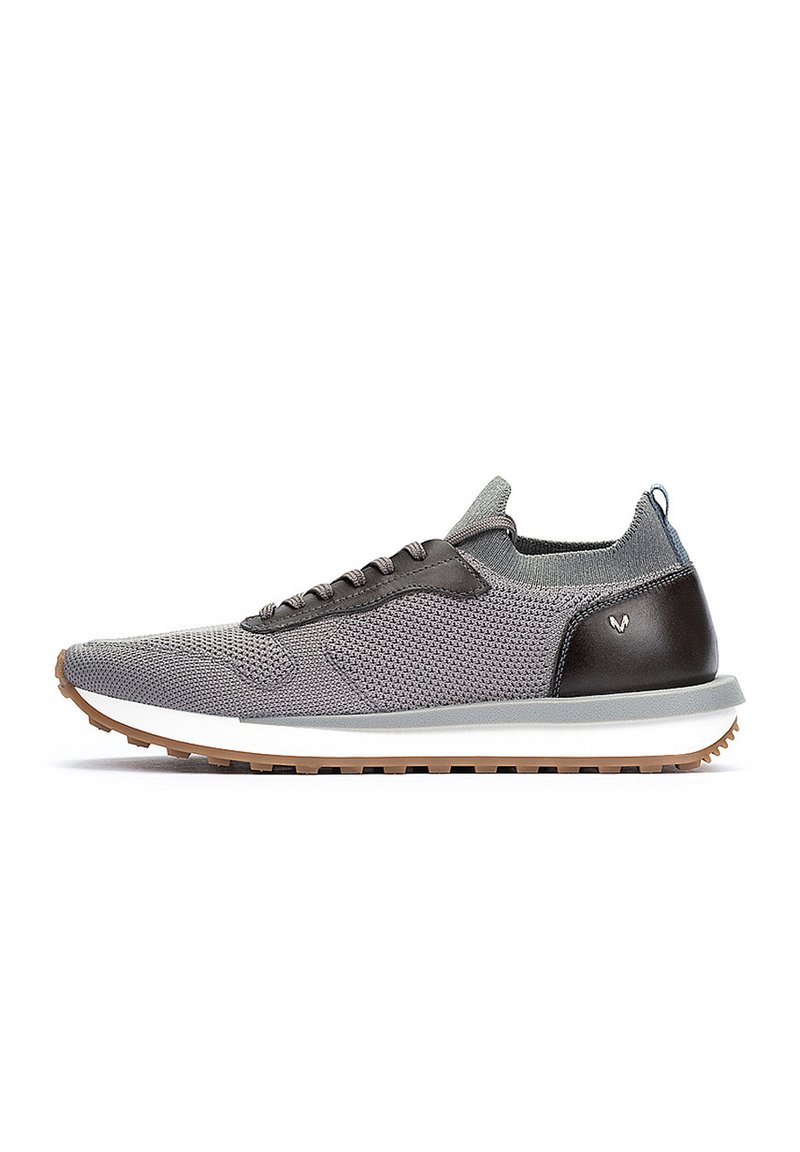 Zapatilla atlética gris de punto con acentos de cuero marrón oscuro, una entresuela blanca y una suela de goma texturizada. Presenta cordones negros y una lengüeta.