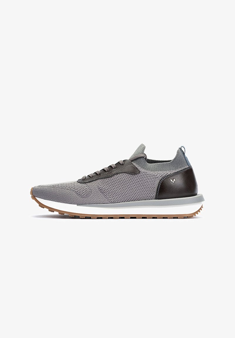 Zapatilla atlética gris de punto con acentos de cuero marrón oscuro, una entresuela blanca y una suela de goma texturizada. Presenta cordones negros y una lengüeta.