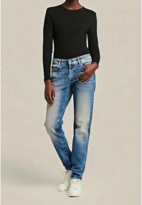 Top nero a maniche lunghe abbinato a jeans denim azzurri leggermente slavati. La modella indossa sneakers bianche, mostrando un outfit casual.