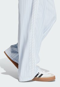 Jasnoniebieskie spodnie w paski o szerokim kroju nogawek i subtelnej fakturze. Połączone z białymi trampkami z czarnymi paskami i gumowymi podeszwami.
