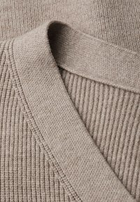 Beiges Strickgewebe mit weicher Textur, bestehend aus gerippten und glatten Bereichen, die am Rand ein markantes Muster bilden.