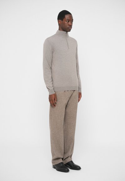 Szürke kötött pulóver magas gallérral és hosszú ujjakkal, bézs struktúrált nadrággal és fekete cipővel párosítva, fehér háttér előtt bemutatva.