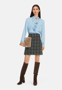 Helles blaues Satinblus mit Rüschen, schwarze und weiße kariertem Rock, braune Wildlederstiefel bis zum Knie und eine beige gesteppte Handtasche.