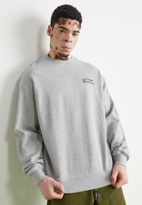 Gray sweatshirt with a crew neck and long sleeves, featuring a small black mountain logo on the left chest. Cotton blend material.
