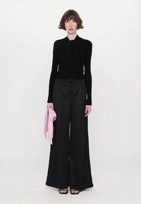 Black long-sleeve top with a bow tie detail, paired with wide-leg black trousers, holding a pink scarf. Minimalist design with smooth textures.