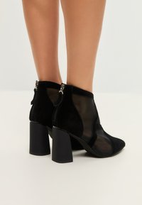 Stivali neri alla caviglia con una combinazione di suede e mesh, punta affusolata e tacchi a blocco robusti, con chiusura a zip sul retro.