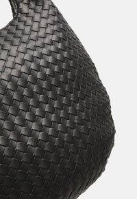 Juodas pintas odinis rankinės suapvalintos formos, pasižyminti tekstūruotu raštu ir glotnia apdaila paviršiuje.