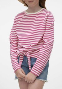 Maglietta a maniche lunghe a righe rosa e bianche con nodo frontale, abbinata a pantaloni corti in denim blu con orli sfilacciati. Sfondo neutro.
