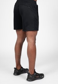 Zwarte sportshorts met een gladde structuur, een elastische tailleband en zijzakken, gecombineerd met zwarte sneakers met gestructureerde accenten.