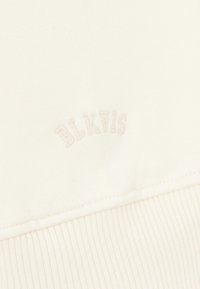 Cream-colored cotton sweatshirt featuring ribbed hem and cuffs, with subtle embroidered "BLK VIS" label in a matching tone.