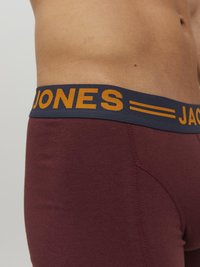 Burgunderfarbene, enganliegende Boxershorts mit einem marineblauen Bund, der "JONES" in orangem Text zeigt. Glattes Baumwollmaterial mit flachen Nähten.