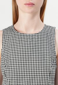 Ein schwarz-weißes Karo-Muster aus Stoff bildet ein ärmelloses Kleid mit Rundhalsausschnitt, das über eine glatte Textur und saubere Nähte verfügt.