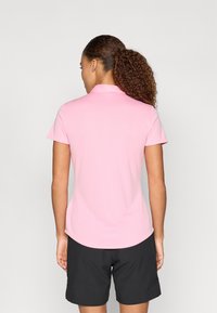 Polo tričko s krátkym rukávom z jemného ružového materiálu, s klasickým golierom a zakriveným spodným lemom, spojené s čiernymi šortkami.