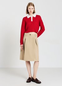 Roter gestrickter verkürzter Pullover mit einem weißen Kragen, kombiniert mit einem beigefarbenen plissierten knielangen Rock und dunkelbraunen Loafers.