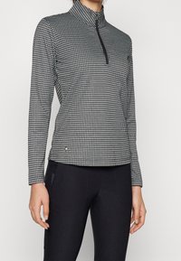Black and white patterned quarter-zip top with a high collar, long sleeves, and smooth fabric texture, paired with black bottoms.