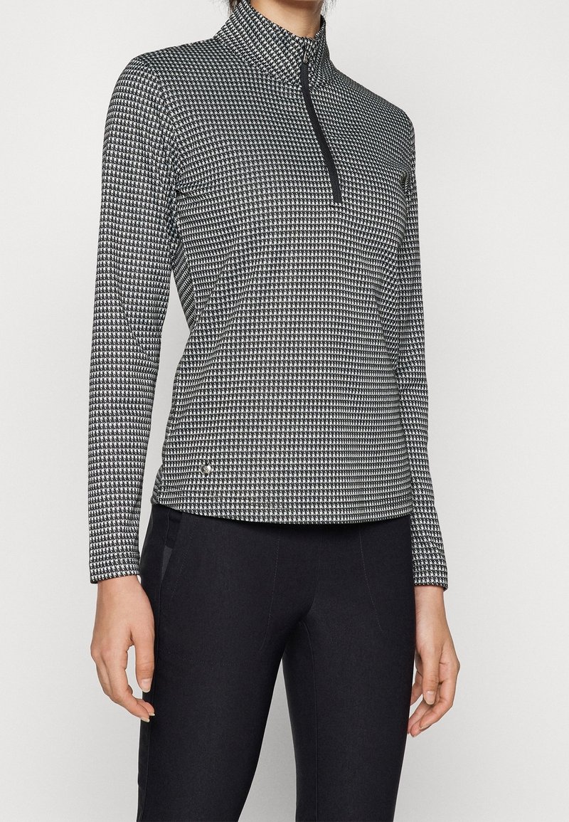 Black and white patterned quarter-zip top with a high collar, long sleeves, and smooth fabric texture, paired with black bottoms.
