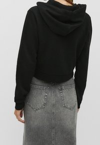 Sweat à capuche noir coupé, avec une capuche, des manches longues et des poignets côtelés. Associé à une jupe en denim grise taille haute avec des poches arrière.