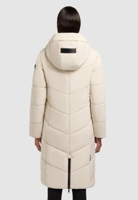 Beige dlouhá péřová bunda s chevron vzorem, kapucí a černým logem. Obsahuje boční kapsy na zip a centrální zadní zip.