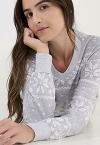 Top gris de manga larga con cuello en V y patrones de copos de nieve blancos en las mangas, confeccionado en una suave tela texturizada.