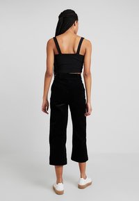 Pantalons en velours côtelé noir à jambe large avec une taille haute, associés à un haut ajusté noir court et des baskets compensées blanches.