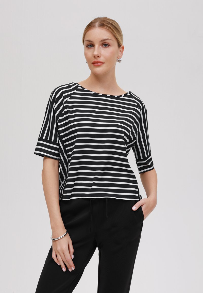 Black and white striped short-sleeve top with a wide neckline, relaxed fit, and textured fabric, paired with black trousers.