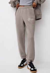 Grå sweatpants med elastisk midja, med "Chicago State of Illinois, USA" tryckt i vitt. Matchas med svarta och vita sneakers.