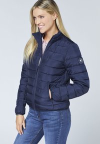 Navy puffer jacket with horizontal stitching, stand collar, zippered front, and side pockets. Soft, smooth texture and lightweight design.