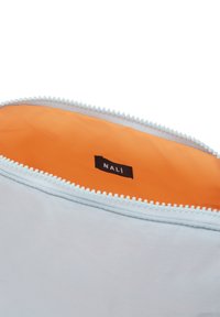 Ljusblå tygväska med vit dragkedjedetalj och orange inredning. Har en svart etikett med texten "NALI" inuti. Slät textur.