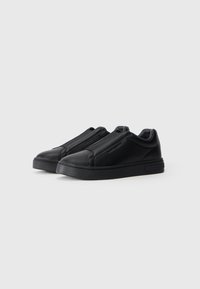 Sapatilhas pretas em couro, estilo slip-on, com uma textura suave, bico redondo e detalhes de costura em contraste, apresentando uma sola de borracha robusta.