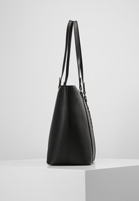 Černá kabelka z hladkého syntetického materiálu, prodloužený trojúhelníkový tvar, dvojité ploché popruhy a viditelné švy jako zdobení.