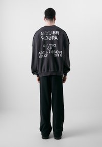 Felpa nera oversize con testo bianco consumato sulla schiena, abbinata a pantaloni neri larghi. Materiale in cotone misto, design casual.