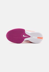 Såle av en sportssko med et lilla og hvitt teksturert grep, en liten Nike swoosh-logo, og oransje detaljer mot en ren hvit bakgrunn.