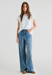 Hvid kortærmet t-shirt parret med højtaljede, brede blå denim jeans med lodrette syninger og en afslappet pasform. Sko med dyreprint.