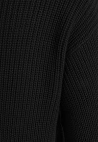 Matériau de pull côtelé noir avec une finition texturée. Présente une couture d'épaule tombante et un tissu doux et extensible. Aucun motif ou accent visible.