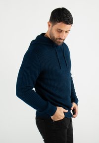 Sweat à capuche en maille côtelée bleu marine avec poche kangourou, capuche à cordon de serrage et tissu texturé. Associé à un jean noir.