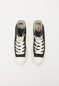 Zapatillas altas de tela oscura con suelas de goma blanca. Presentan cordones blancos, costuras en contraste y un cuello acolchado.