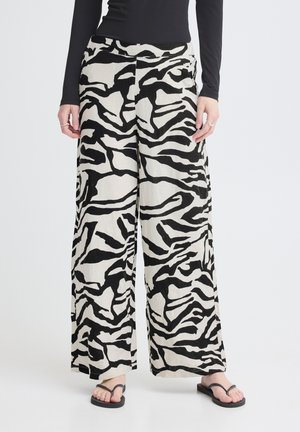 Bukser med vide ben med sorte og hvide abstrakte zebra-striber, båret med sort langærmet top og sorte flip-flops.