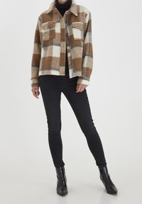 Hnědá a krémová károvaná flanelová bunda se dvěma předními kapsami, zapínáním na knoflíky, měkkou strukturou a klasickým límcem, zkombinovaná s černými skinny džíny.