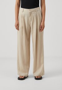 Beiga vida byxor gjorda av lätt tyg, med framfickor, vanlig midja och avslappnad passform, matchade med svarta sandaler.