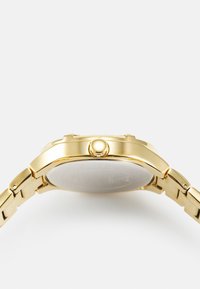 Guldmetalur ur med en rund kasse og en glat bezel. Remmen består af sammenkoblede guldsegmenter med en blank finish.