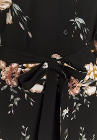 Schwarzes Blumenkleid mit einem Bindegürtel, Knopfdetails und weichem Stoff, der eine Mischung aus hellrosa, weiß und grünen Blumendesigns zeigt.