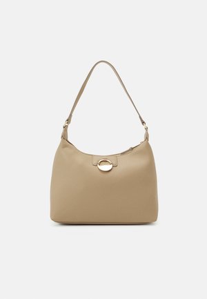 Sac à bandoulière en cuir beige avec une seule sangle et un fermoir circulaire doré sur un fond clair uni.