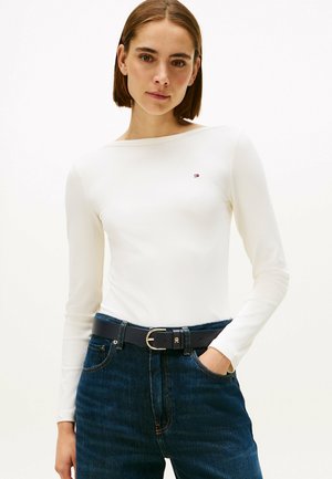 Witte geribbelde long sleeve top met een brede halslijn en een klein logo detail, gecombineerd met donkerblauwe denim jeans en een zwarte riem met een gouden gesp.