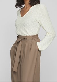 Haut à manches longues texturé crème avec un col en V, associé à un pantalon marron ample taille haute avec une ceinture nouée.