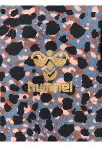 Blauer Stoff mit einem Leopardenmuster in Schwarz-, Braun- und Rosatönen. Mit einem glänzenden goldenen Logo "hummel" in der Mitte.