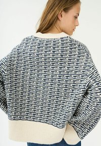 Maglione lavorato a maglia con un motivo geometrico blu navy e crema, caratterizzato da un colletto rotondo e orlo a coste. Texture morbida, design oversize.