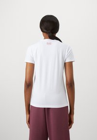 Maglietta bianca in cotone con un design aderente, maniche corte e un piccolo logo rosa sul retro. Texture liscia e silhouette classica.