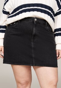 Jupe en jean noir avec une coupe ajustée, fermeture à boutons à l'avant et passant de ceinture. Le tissu a une légère élasticité et une texture lisse.